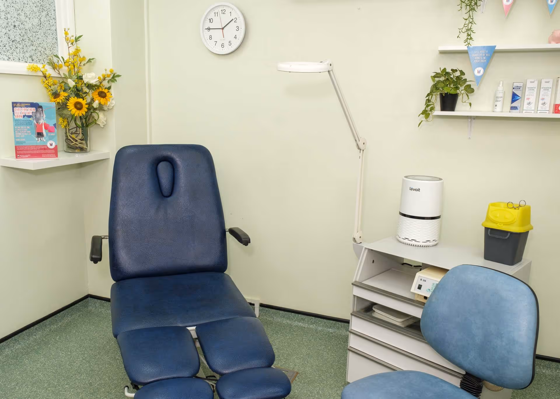 A medical examination room with an adjustable chair, a clock, and a lamp.
