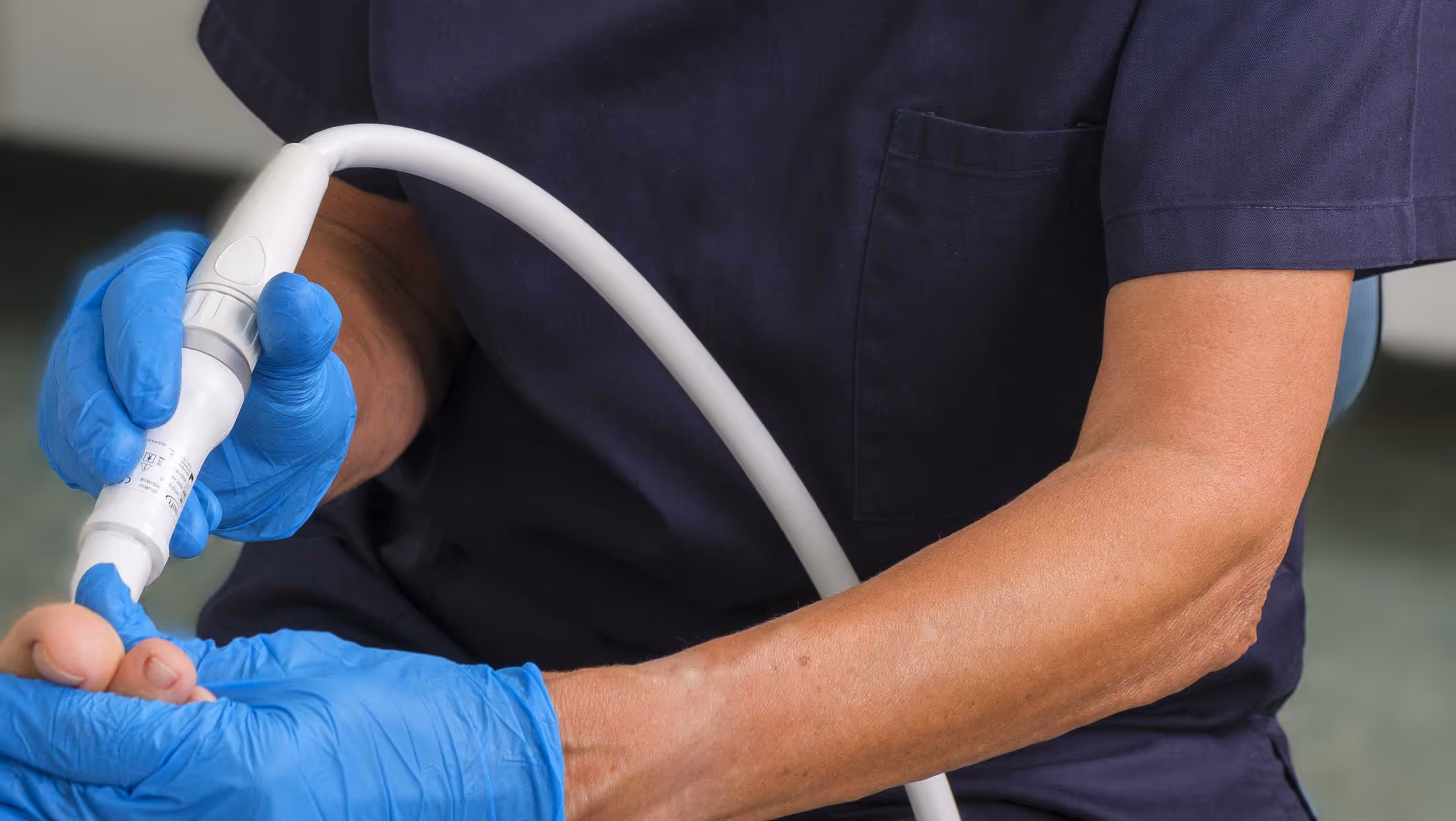 A person in gloves uses a tool to treat a patient's foot.